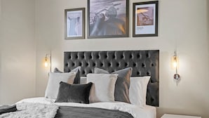 A bedroom with a tufted headboard, a bed with multiple pillows, and two wall-mounted light fixtures.