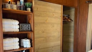 A wooden room with a bed, shelves with folded towels, a sign, and a plant. - Barnaminium Upstairs Loft (Pickens)