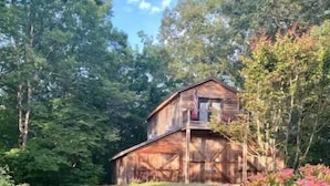 A rustic wooden cabin with a balcony, surrounded by lush greenery and flowering plants. - Barnaminium Upstairs Loft (Pickens)