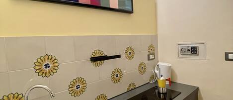 A kitchen with a modern design, featuring a black countertop, a sink, a coffee machine, and a decorative tile backsplash with floral patterns.
