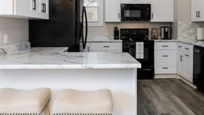 A modern kitchen with white cabinetry, a black refrigerator, a microwave, and a large island with bar stools. - The Alley House - 4BR with Hot Tub (Columbus)