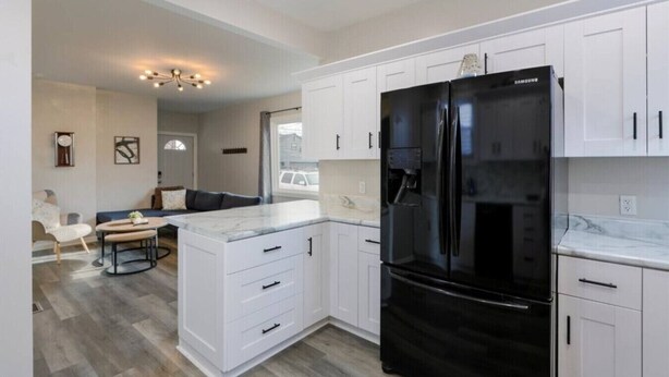 A modern kitchen with white cabinetry, a black refrigerator, and a marble countertop. - The Alley House - 4BR with Hot Tub (Columbus)
