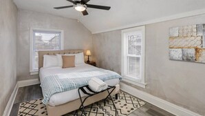 A bedroom with a bed, a ceiling fan, a window, and a wall art piece. - The Alley House - 4BR with Hot Tub (Columbus)