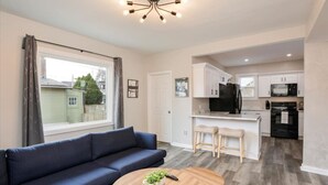 A modern apartment with a sofa, a round wooden table, a kitchen with white cabinets, a black refrigerator, and a microwave. - The Alley House - 4BR with Hot Tub (Columbus)