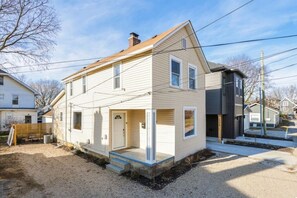 Uma casa de dois andares com varanda frontal, porta de garagem visível e pequeno jardim da frente.