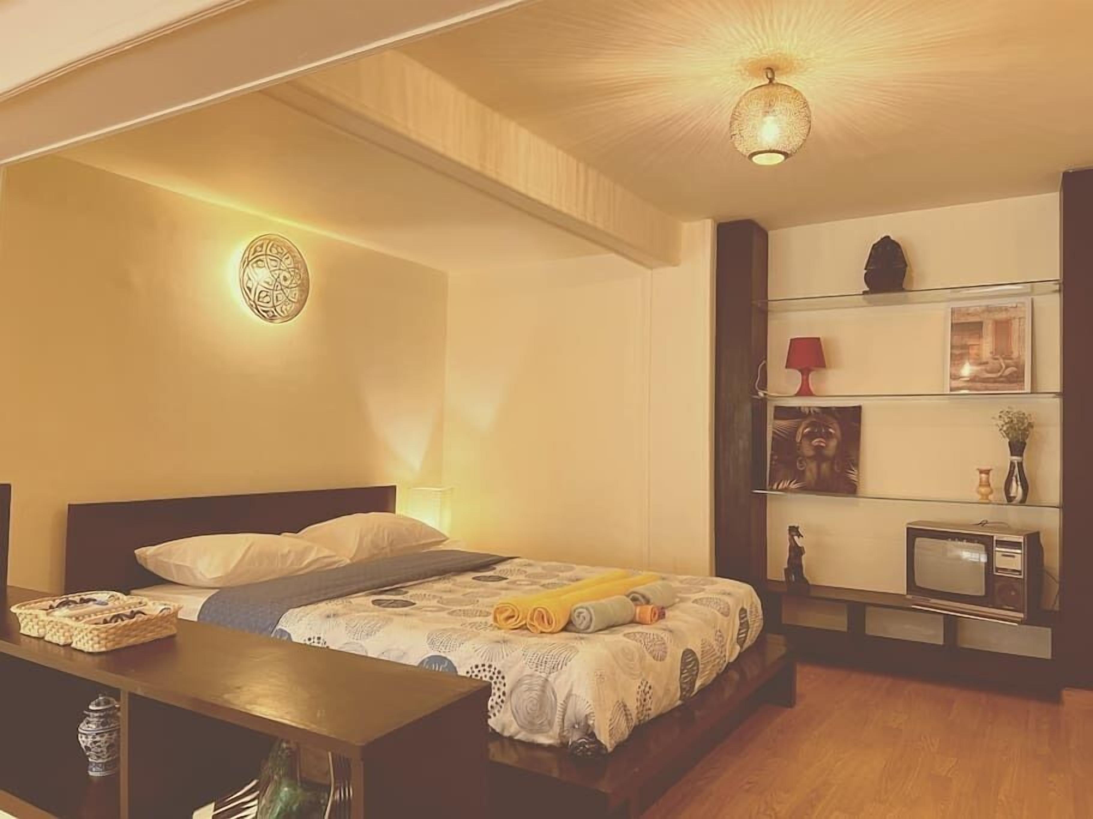 A bedroom with a bed, bedside table, lamp, and a shelf with decorative items.