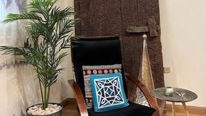 A wooden chair with a black cushion and a geometric pillow, placed in front of a decorative wooden panel. - Vintage Vibrant Space ! (Cairo)