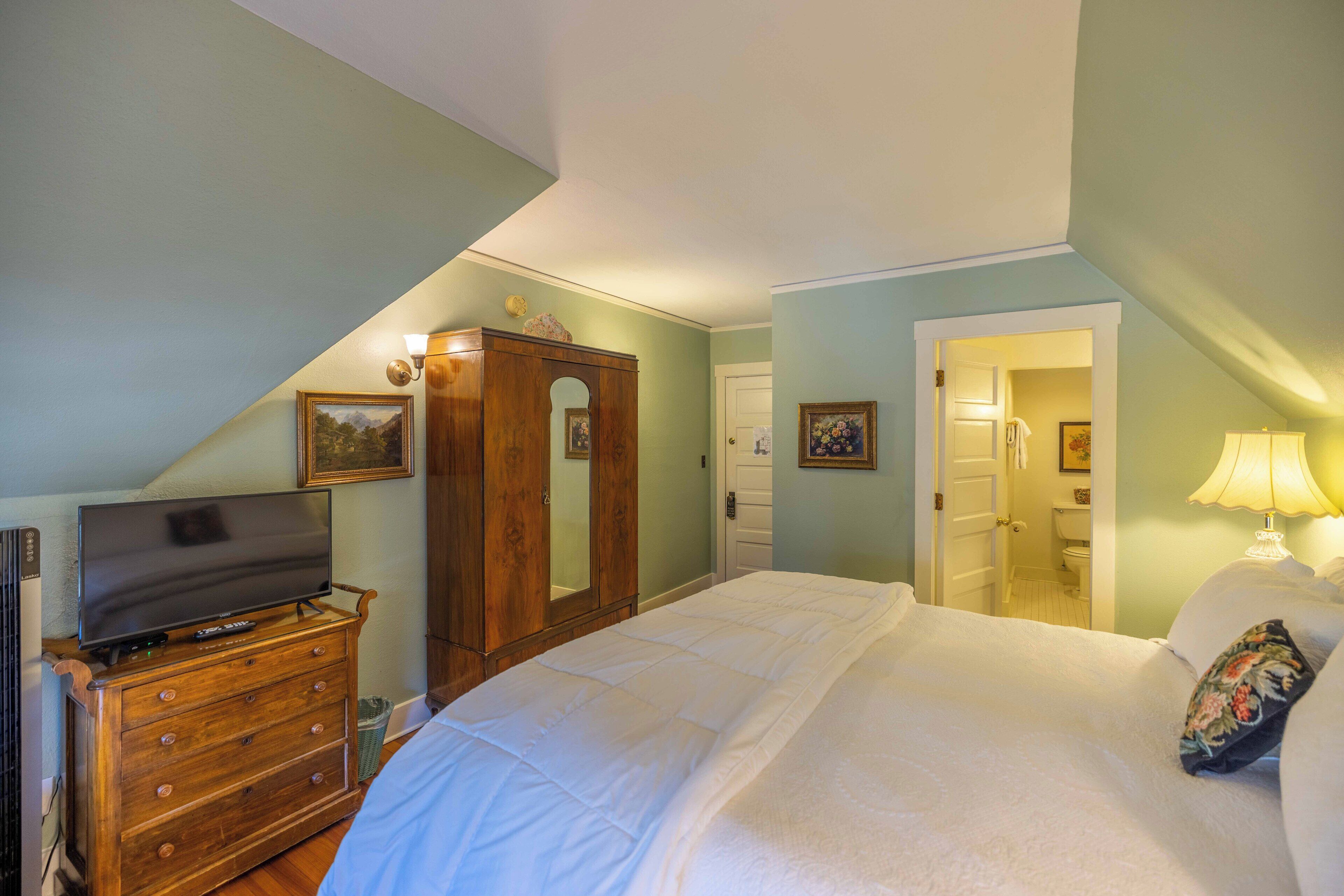 A bedroom with a bed, dresser, TV, and a door leading to a bathroom.