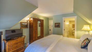 A bedroom with a bed, dresser, TV, and a door leading to a bathroom.