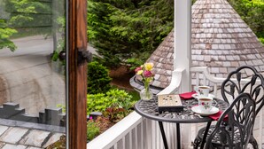 Un balcon avec une table, des chaises, un vase de fleurs et une vue sur un jardin et un bâtiment.