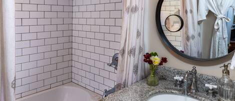 A bathroom with a white tiled shower, a sink with a marble countertop, and a round mirror.