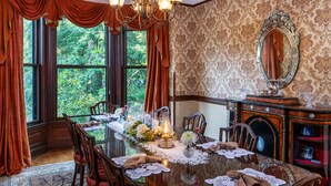Une salle à manger avec une grande table dressée pour six personnes, entourée de chaises, et un lustre au-dessus.