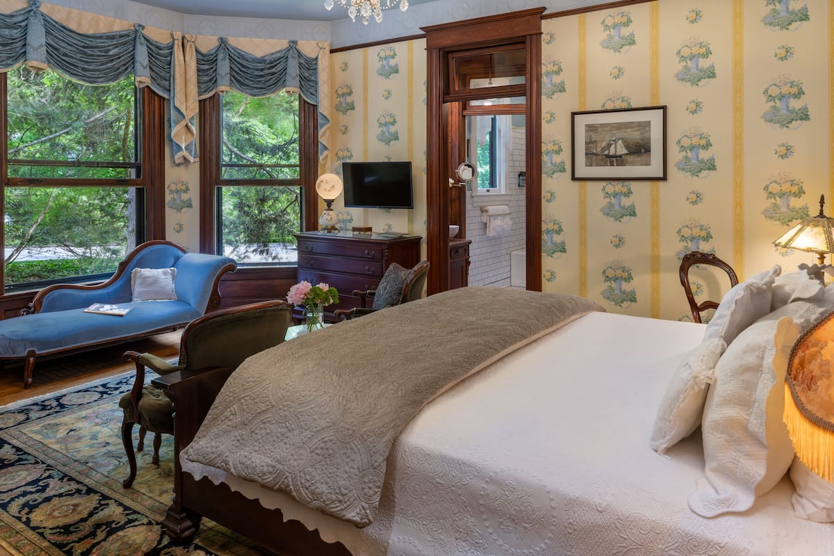 Une chambre à coucher avec un grand lit, un fauteuil bleu, une commode en bois et un téléviseur.