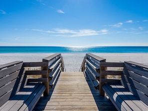 En træbro, der fører til en strand med en klar blå himmel.