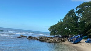 A beach with clear blue water, rocky shore, and a few boats. - Hotel Green Mountain Cahuita  (Cahuita)