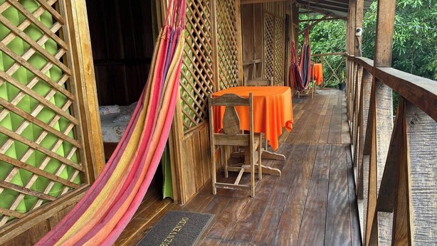 A wooden deck with a hammock, a table with an orange tablecloth, and a wooden chair. - Hotel Green Mountain Cahuita  (Cahuita)