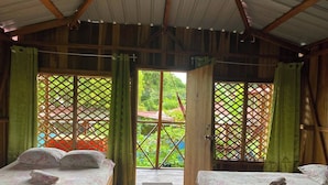 A room with two beds, wooden flooring, and a view through a lattice door. - Hotel Green Mountain Cahuita  (Cahuita)
