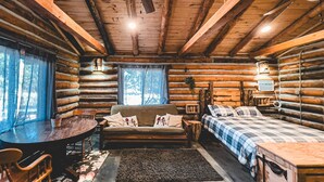 A log cabin interior with a sofa, a bed, a table, and a chair.