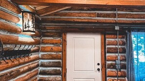 A log cabin interior with a wooden door, a bench, and a wall-mounted light fixture.