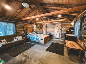 A log cabin interior with a bed, sofa, and dining table. - The Settlers Cabin Retreat (Monticello)