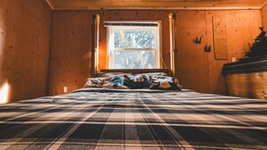 Quarto com cama, janela e paredes de madeira.