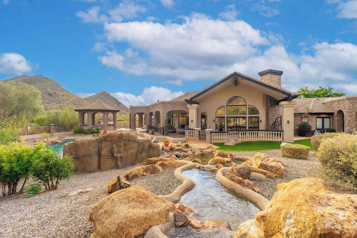A large house with a swimming pool, a rock garden, and a mountain in the background.