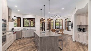 A modern kitchen with a central island, built-in appliances, and large windows offering views of greenery. - Scottsdale Diamond Mtn Oasis+Waterslide+Pickleball (Scottsdale)