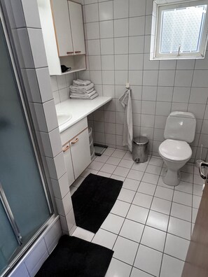 Een kleine, schone badkamer met witte tegels, een toilet, een wastafel en een raam.