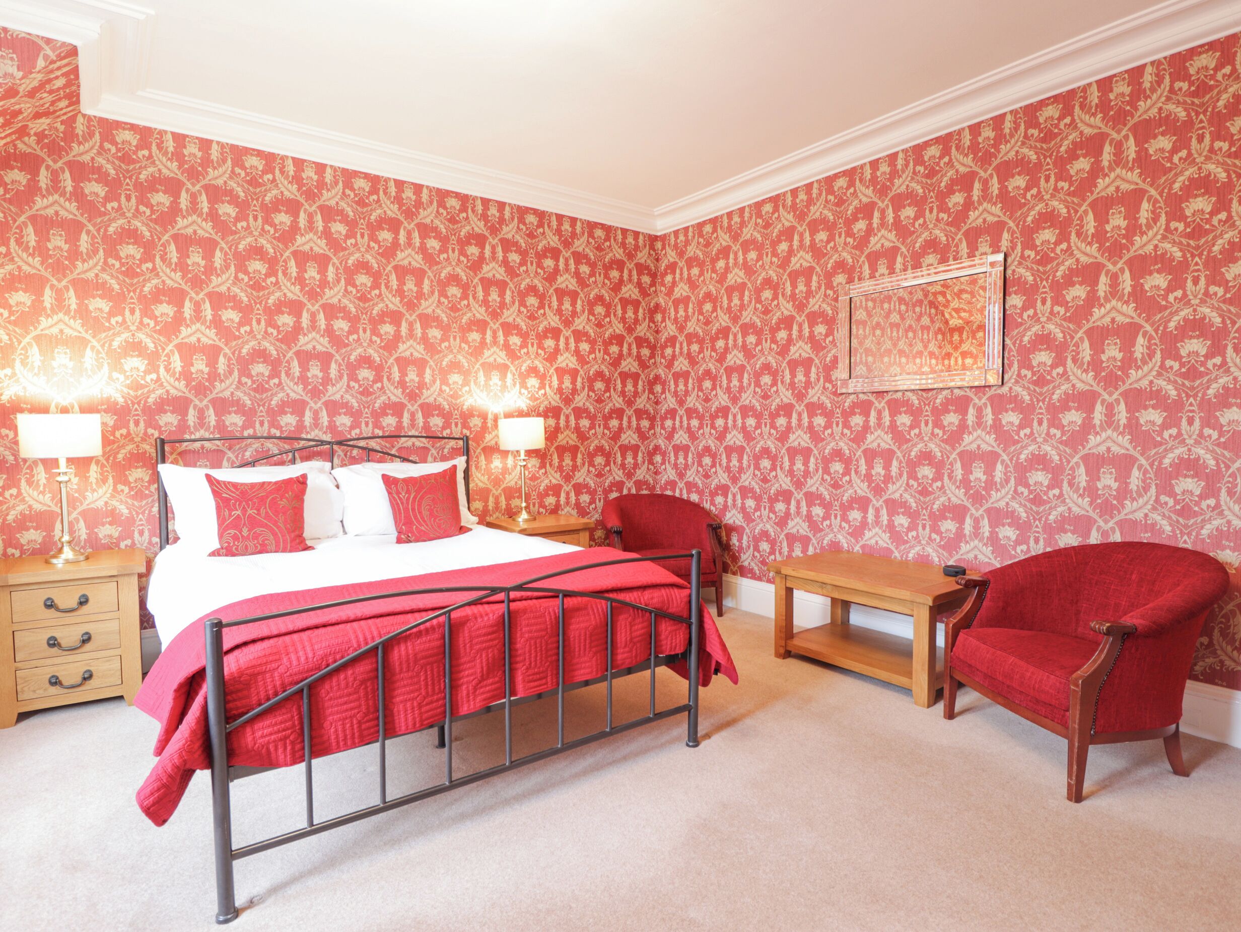 A bedroom with a bed, two bedside tables with lamps, a wooden bench, and a red armchair.