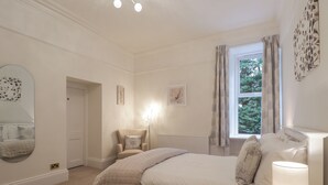 Ein Schlafzimmer mit Bett, Nachttischlampe, Stuhl und einem Fenster mit Vorhängen.