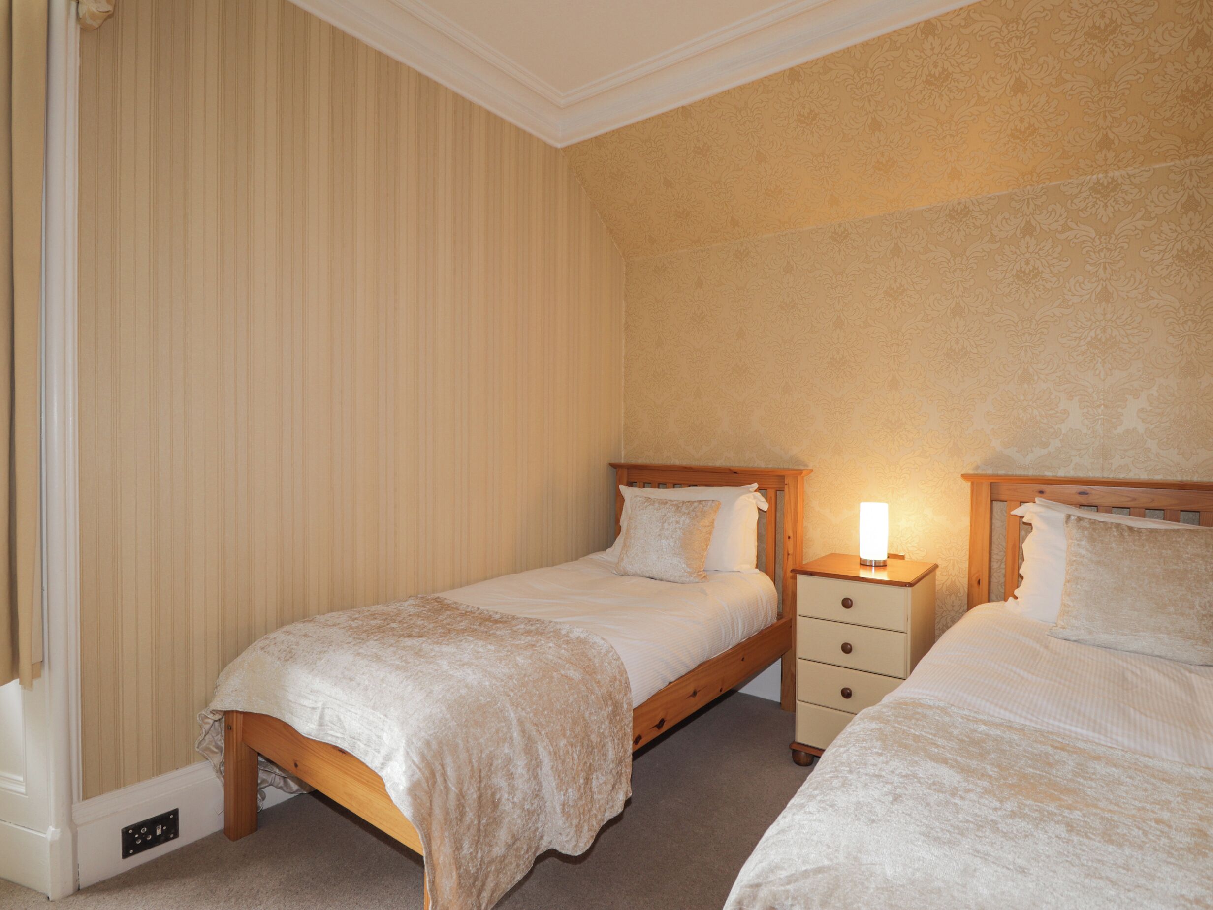 A bedroom with two single beds, a nightstand with a lamp, and a wall with a floral pattern.