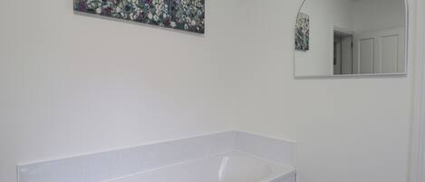 Une salle de bain avec une baignoire blanche, un miroir fixé au mur et un tableau représentant des fleurs.