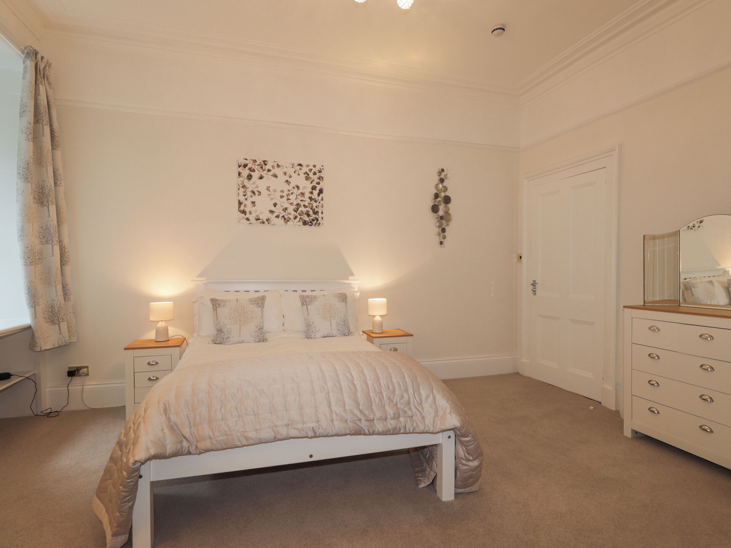 A bedroom with a bed, bedside tables, a dresser, and a door.