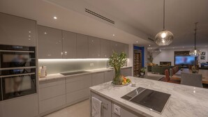 A modern kitchen with a marble countertop, built-in oven, and a dining area with a TV and seating.