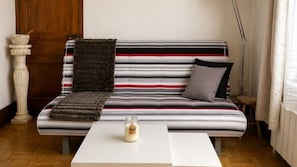 En stribet sofa med et pelskast, et lille bord med et lys og en trægulv.