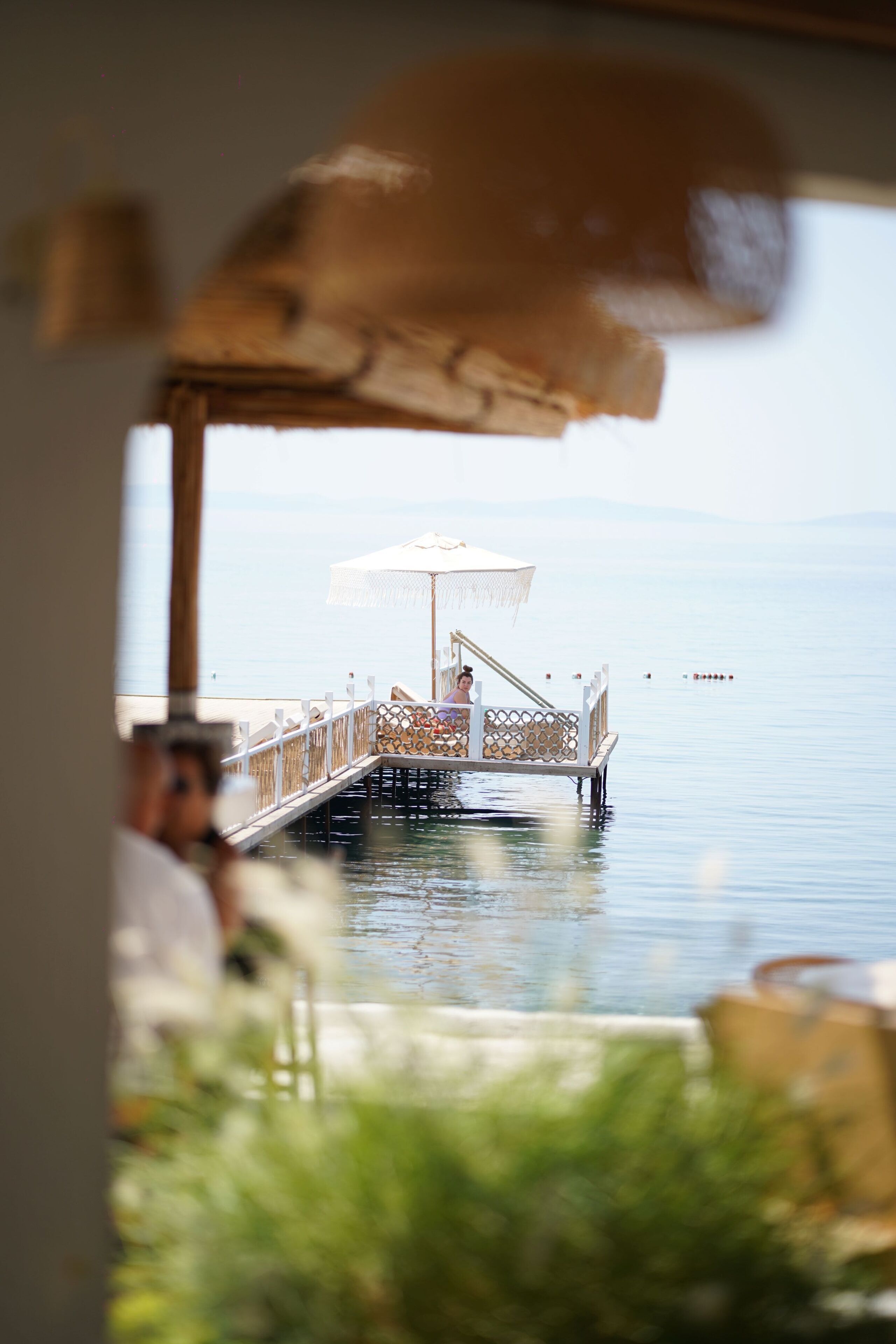 A pier extending into calm waters with a covered seating area and a person sitting at the end.