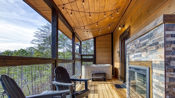 A wooden deck with Adirondack chairs and a fireplace, overlooking a forested area.