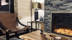 A cozy living room with a leather chair, a wooden coffee table, a lamp, and a fireplace.