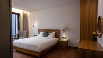 Ein modernes Hotelzimmer mit einem großen Bett, einem Holzkopfteil, Nachttischen und Blick auf die Stadt durch ein großes Fenster.