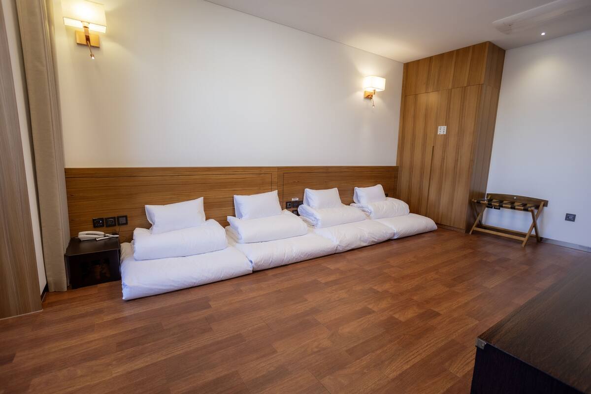 A hotel room with a large bed, wooden headboard, two bedside tables, and a bench by the window.