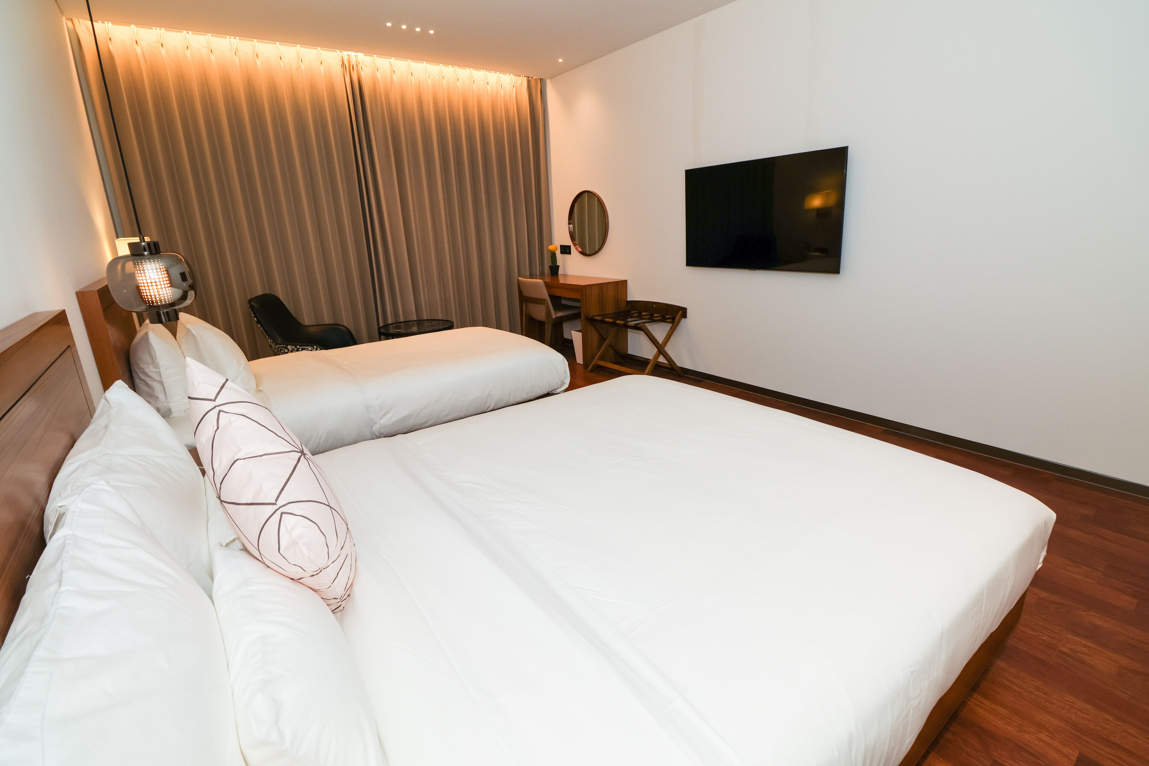 A hotel room with two beds, a desk, a chair, a TV, and a large window with curtains.