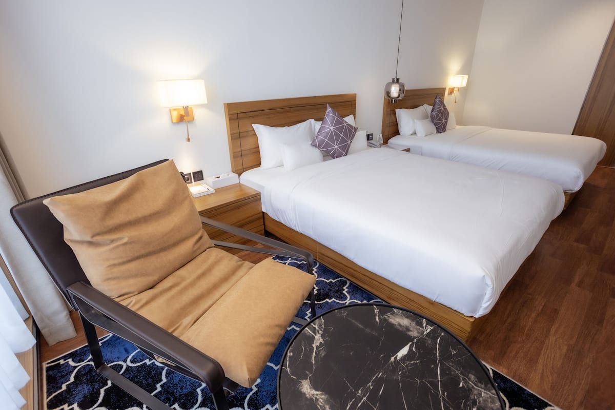 A hotel room with a single bed, a chair, a small table, and two bedside lamps.