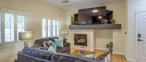 A living room with a sofa, a flat-screen TV mounted on a wall, a fireplace, and a door.