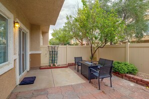 Um pátio externo com mesa e cadeiras, uma pequena área de jardim e vista para o bairro ao redor.