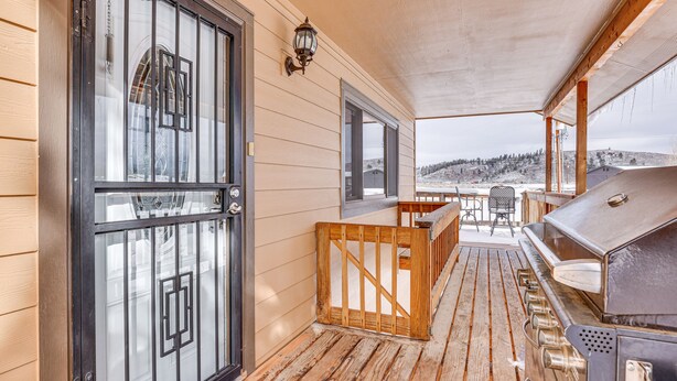 Un espace extérieur abrité, doté d’une terrasse en bois, d’un barbecue et offrant une vue sur un paysage enneigé.