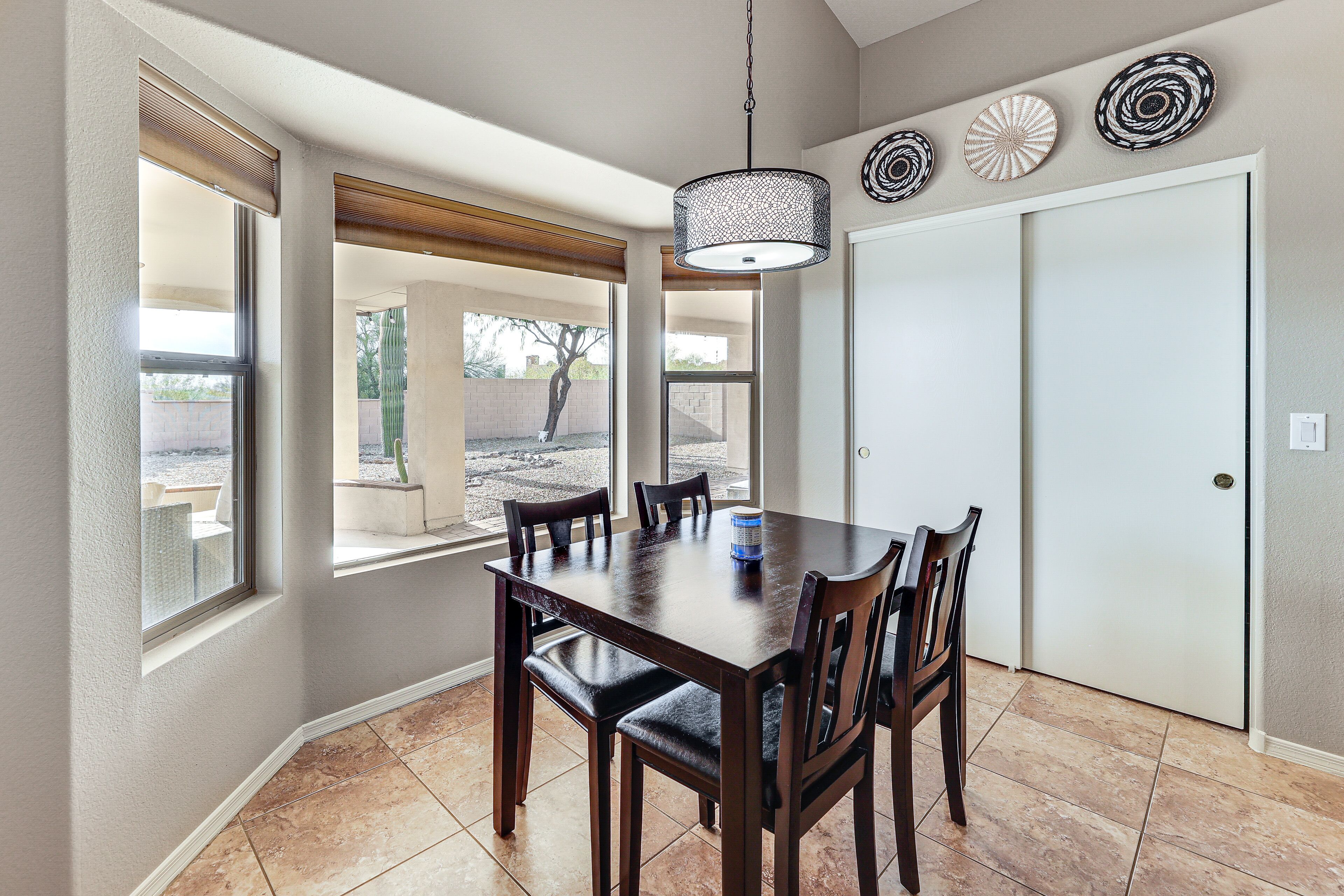 A dining area with a wooden table and chairs, a hanging light fixture, and a view of the outdoors through large windows.