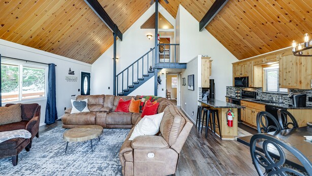 A spacious living area with a large brown sectional sofa, a dining table with chairs, a kitchen with wooden cabinets, and a staircase leading to an upper level. - Serene Cabin Retreat Between Murphys & Arnold (Murphys)