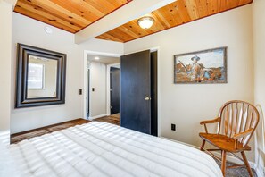 A bedroom with a large bed, a wooden rocking chair, a painting on the wall, and a door leading to another room. - Serene Cabin Retreat Between Murphys & Arnold (Murphys)