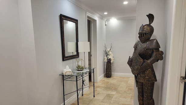 Un couloir avec une console en verre, un miroir, un vase de fleurs blanches et une statue de chevalier.