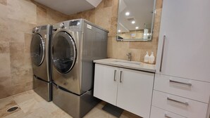 Une salle de bain moderne dotée d’un lave-linge et d’un sèche-linge intégrés, d’un grand miroir et d’un meuble-lavabo blanc avec des tiroirs.